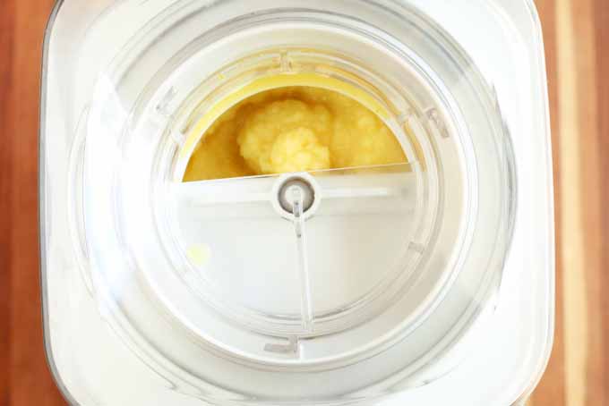 Top-down view of a Cuisinart ice cream maker that is freezing and mixing a batch of orange sherbet, on a wood background.