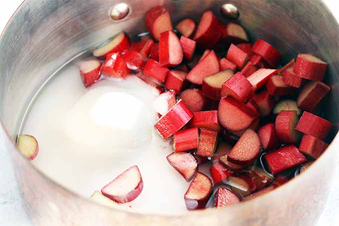 Closeup of a saucepan filled with chopped rhubarb, water, and sugar to make a sauce.