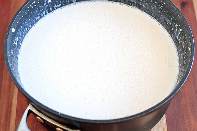 White bubbly ice milk base before freezing, in a large black saucepot, on a brown wood surface.
