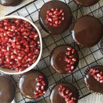 Horizontal image of a cooling rack with cupcakes with ganache and pomegranate seeds.