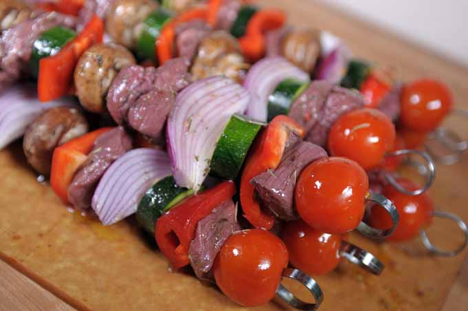 Cherry tomatoes, red bell pepper, zucchini, mushrooms, onion, and lamb meat placed on skewers, ready to be grilled.
