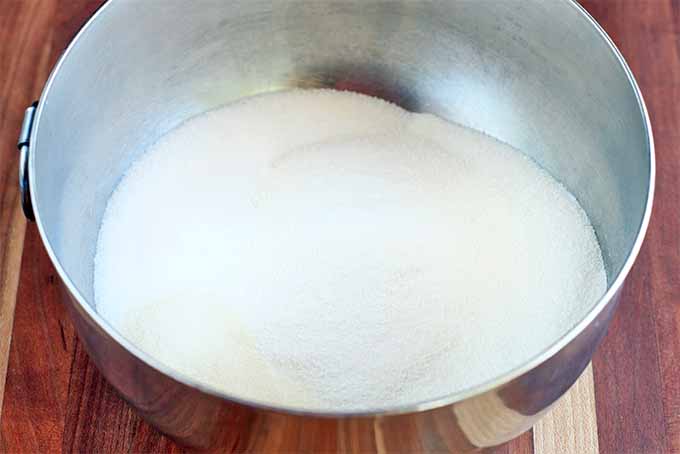 A stainless steel bowl of the mixed dairy base mixture used to make a frozen dessert, on a brown wood background.
