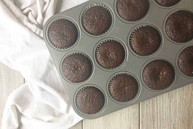 Horizontal image of a white towel underneath a tray with baked cupcakes.