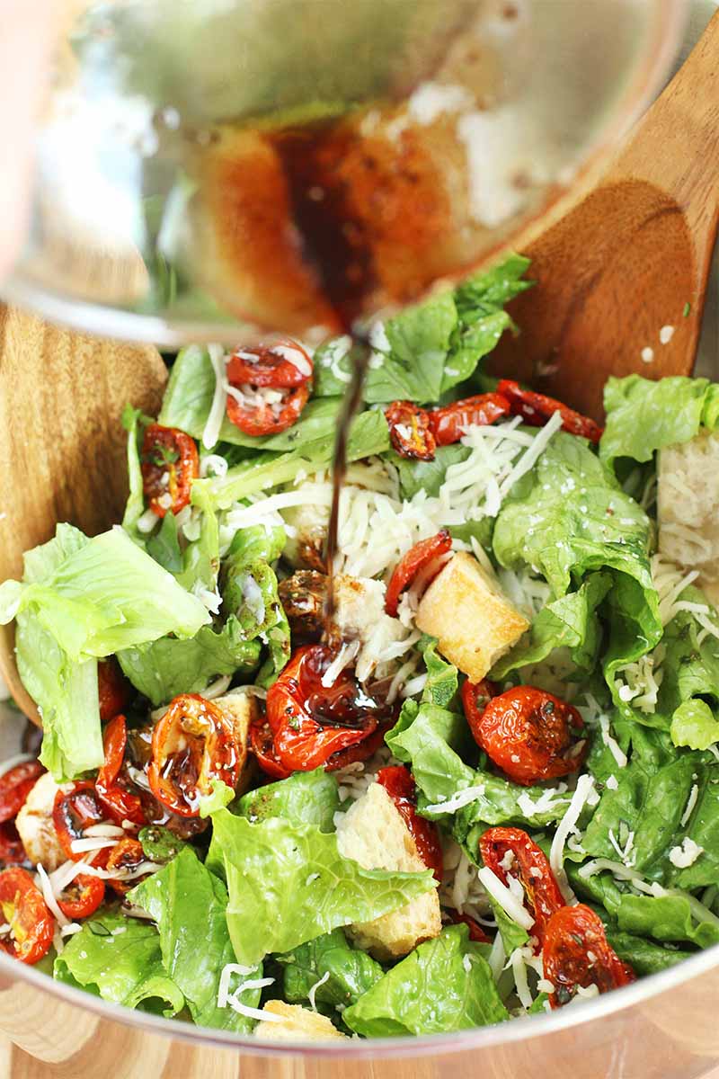 Vertical closeup of panzanella in a large mixing bowl with two wooden spoons.