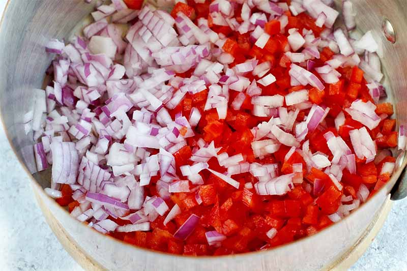 Chopped red onion and red bell pepper in the bottom of a saucepan.