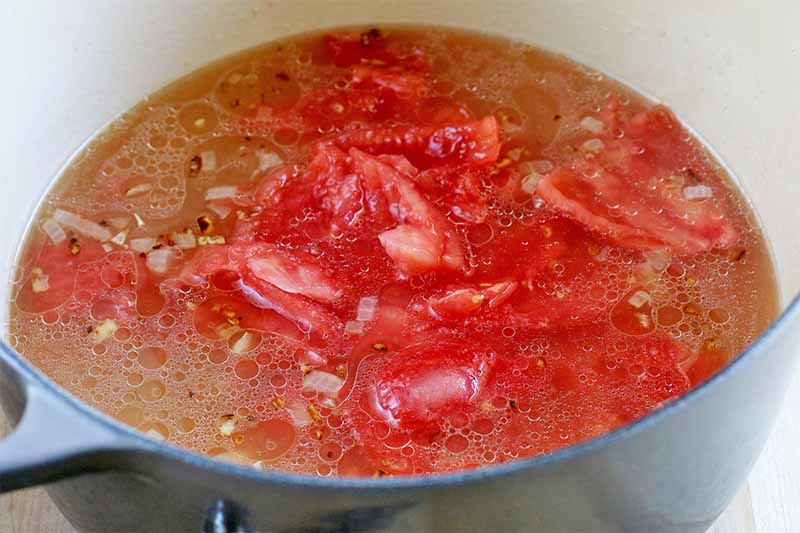 Fresh tomatoes and chicken broth in a white and blue stock pot.
