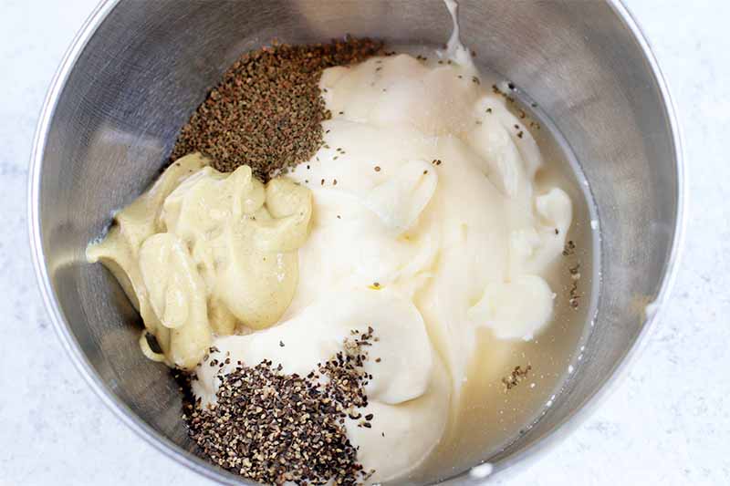 A large stainless steel bowl of mayonnaise, Dijon mustard, celery seed, ground black pepper, and vinegar.