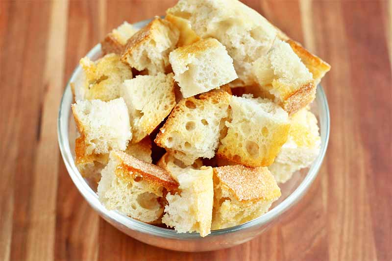 Chunks of sourdough bread in a small white bowl, on a brown wood background.