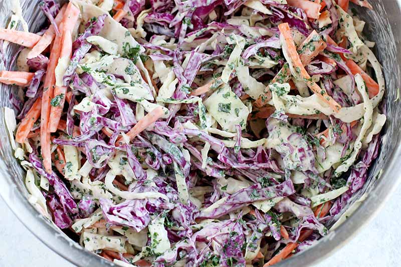 Top-down closeup of a stainless steel mixing bowl of homemade coleslaw with a white dressing.