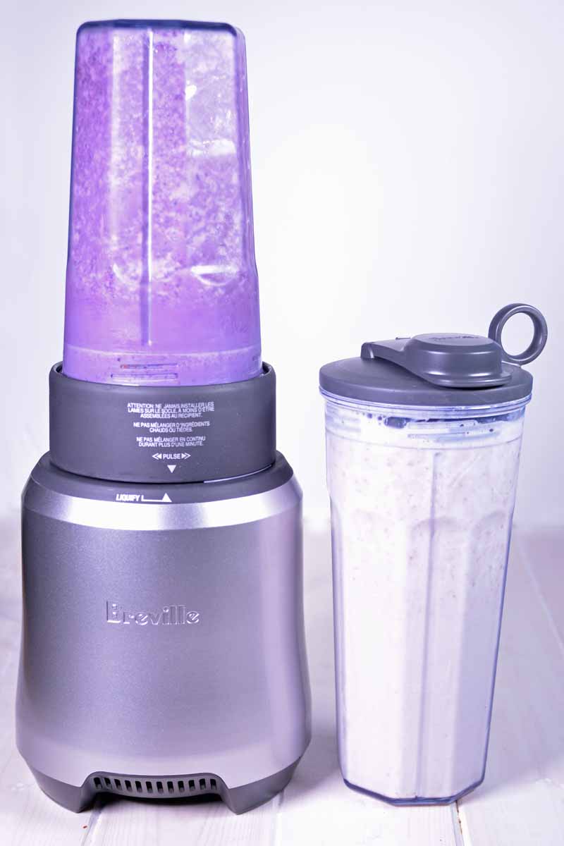 The Breville Boss To Go Personal Blender with one container full of blueberry smoothie and the other of a strawberry smoothie mixture.