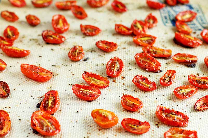 Roasted grape tomatoes on a white nonstick silicone baking mat.