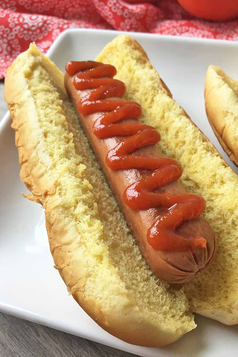 Vertical closeup image of a hot dog with ketchup.