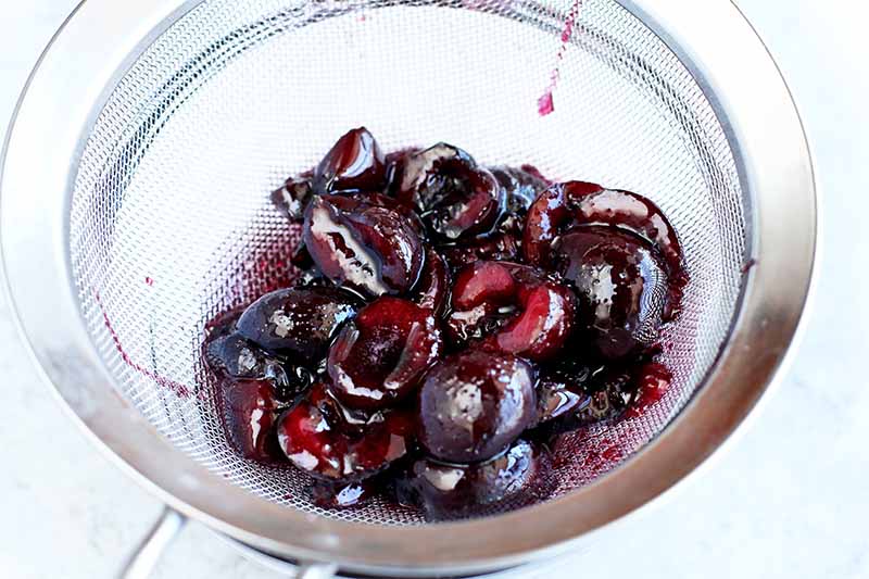 Black cherries cut in half in a glass bowl with pink syrup.
