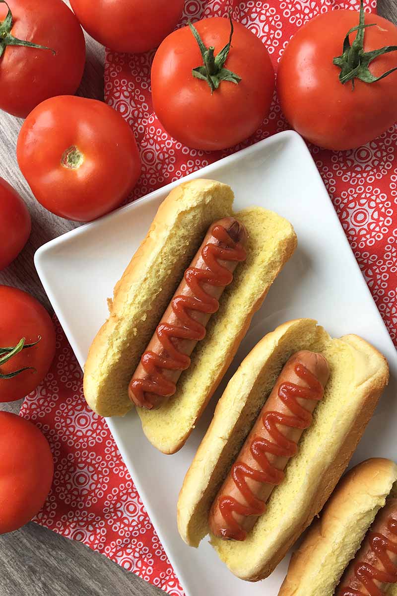Vertical image of hot dogs on a white platter with tomatoes. 