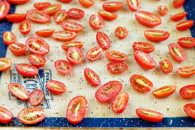 Halved grape tomatoes on a nonstick silicone baking mat, sprinkled with salt and pepper.
