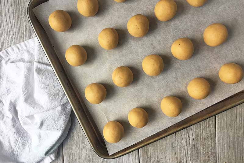 Horizontal image of a baking sheet with yellow dough balls.