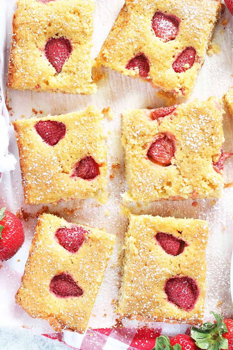 Top-down shot of six square slices of strawberry cake with a few scattered whole berries.