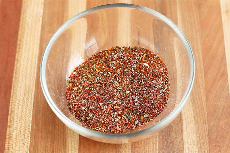 Homemade taco spice seasoning mix in a glass bowl, on a striped wood background.