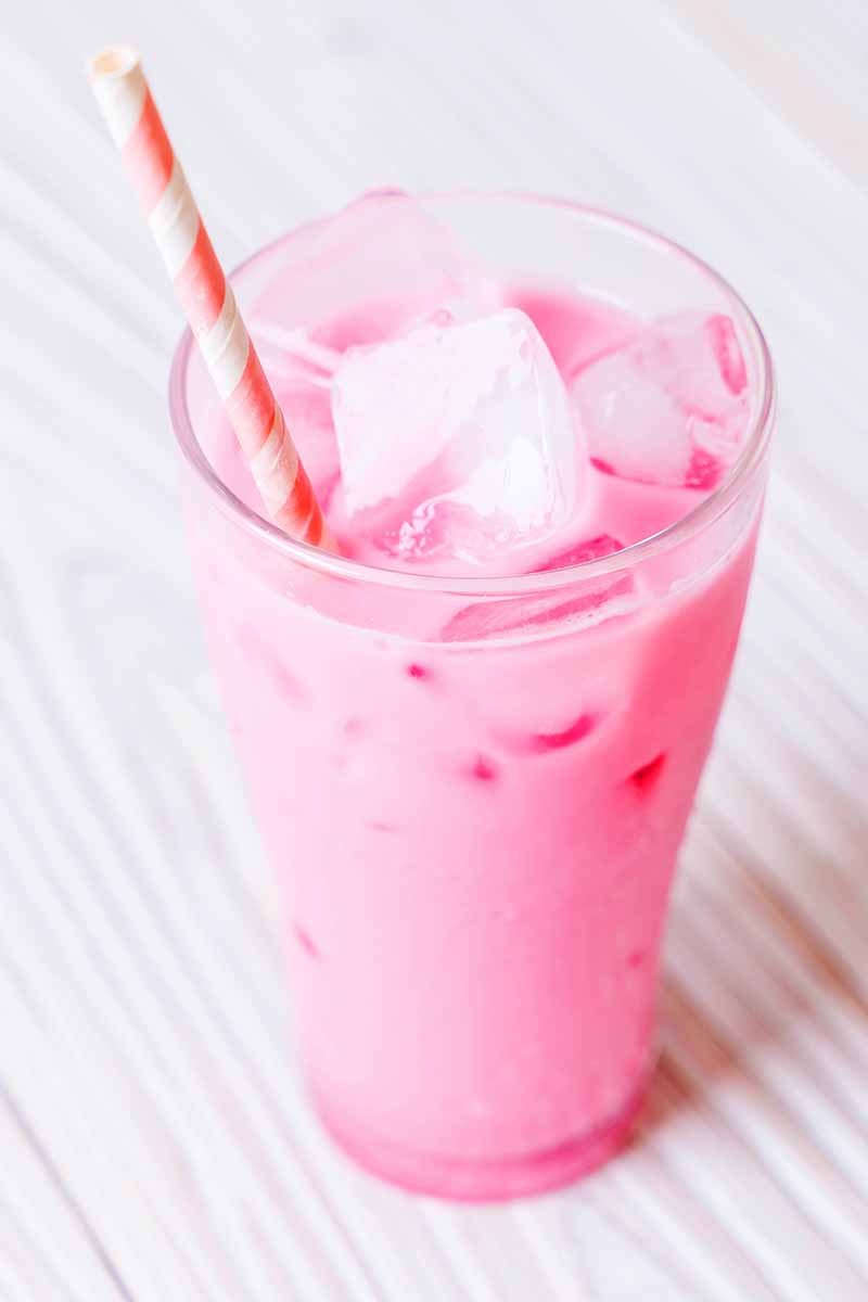 Vertical image of a pink shake in a clear glass, with ice cubes floating on top, and a red and white striped straw.