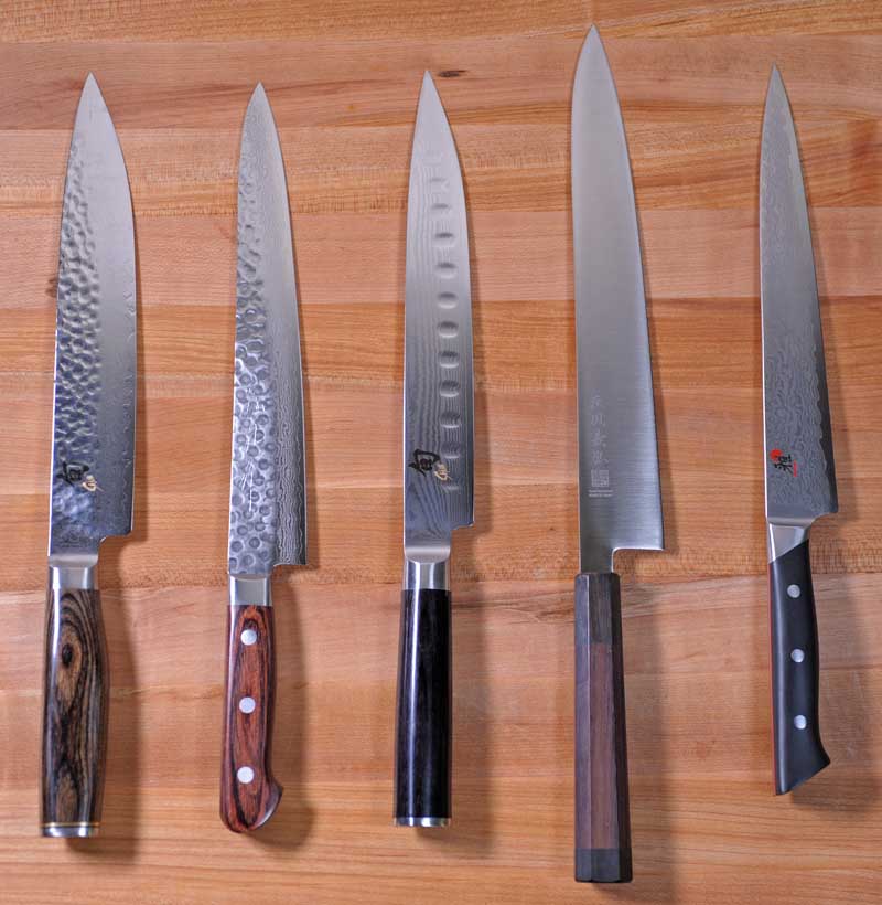 Five different Sujihiki knives on a maple cutting board.