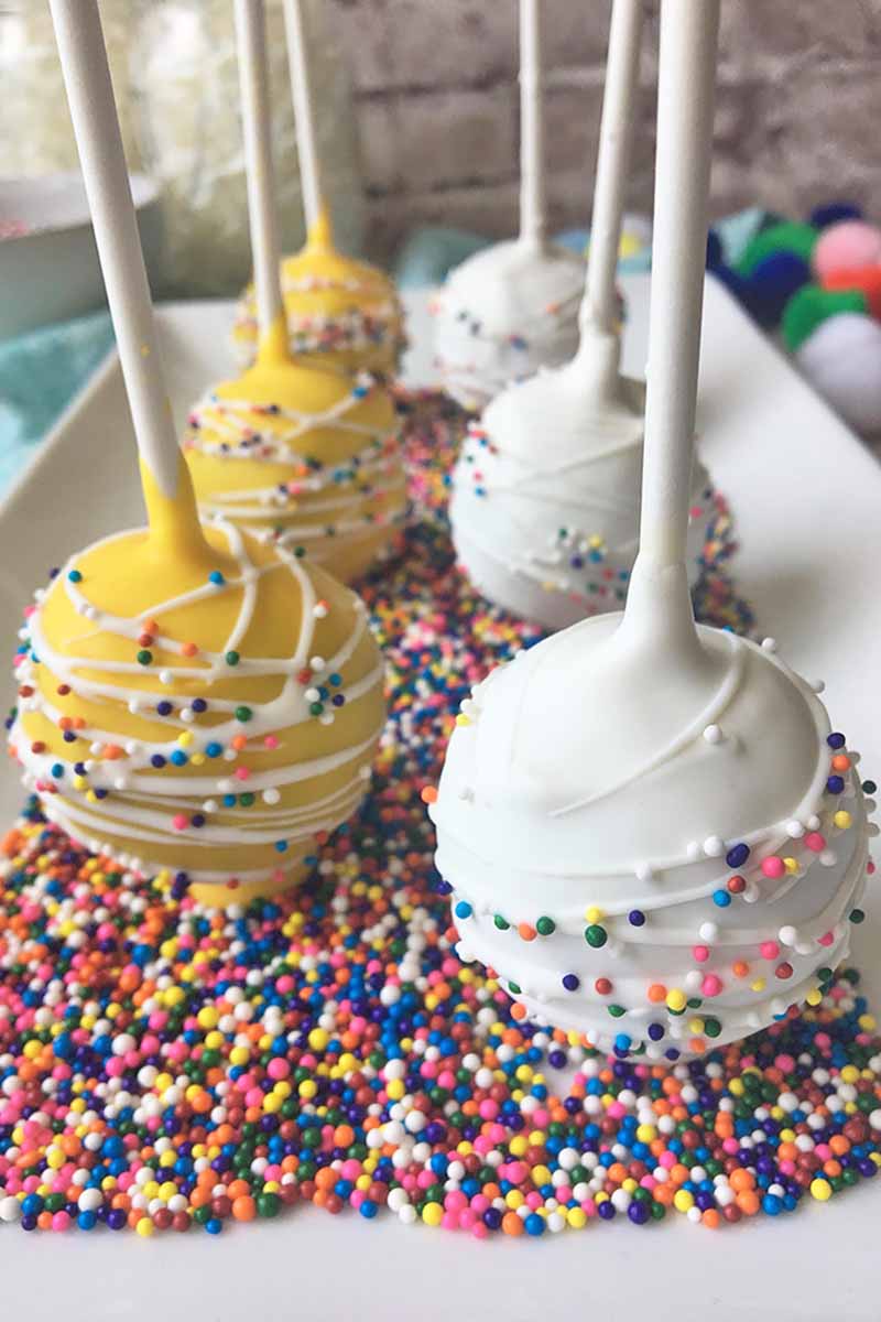 Yellow and white pops on a plate of rainbow sprinkles.