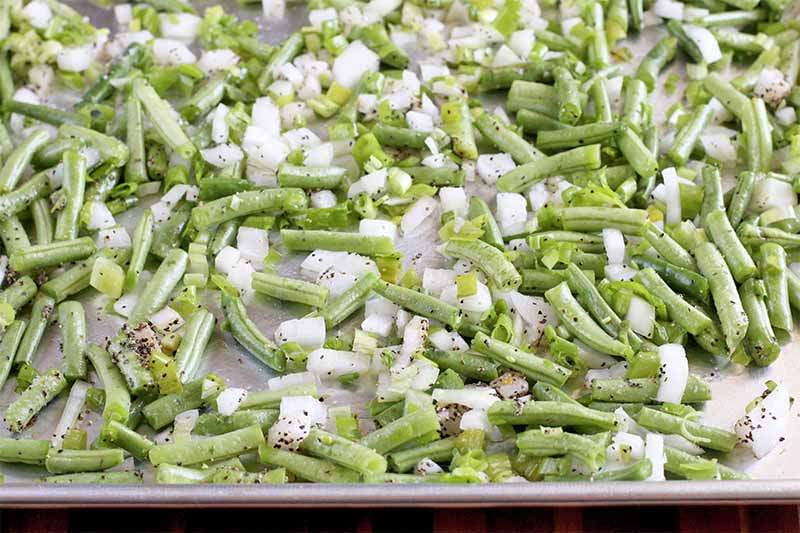 Chopped green beans and white onions are spread in a single layer on a silver metal sheet pan.