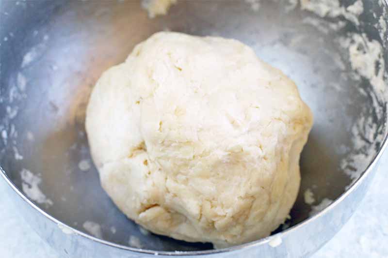 A ball of pie crust dough in a stainless steel mixing bowl.