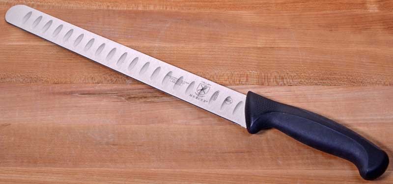 Mercer Culinary Millennia Granton 11-inch Slicing Knife on a maple wood cutting board.