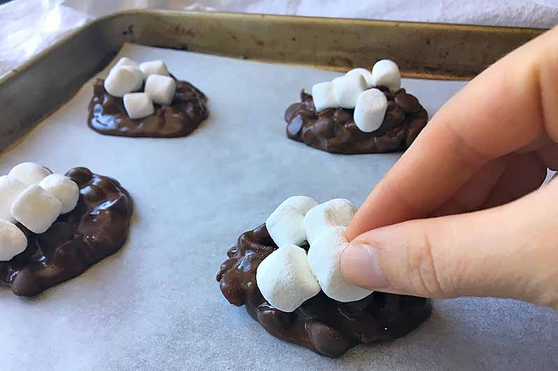 Horizontal image of placing mini marshmallows on top of cookie mounds.