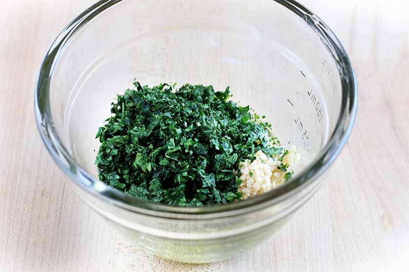 A glass bowl of chipped cilantro and minced garlic.