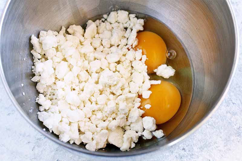 Crumbled goat cheese and eggs in a stainless steel mixing bowl.