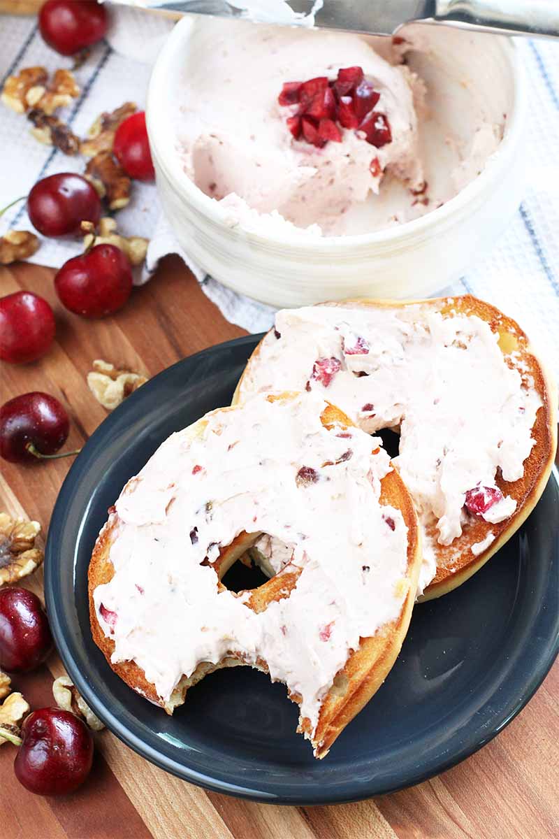 Vertical image of two bagel slices, one with a bite taken out of it, spread with cherry cream cheese.