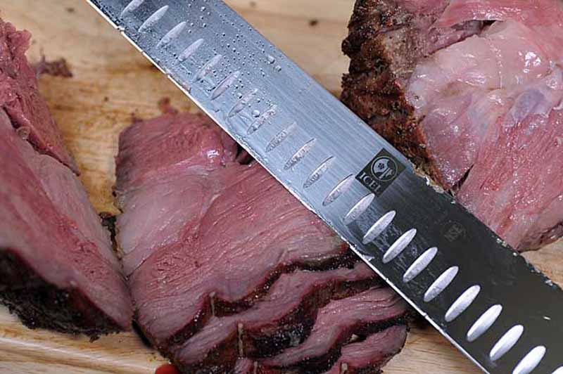 An icel slicing knife trimming off slices of a standing rib roast.