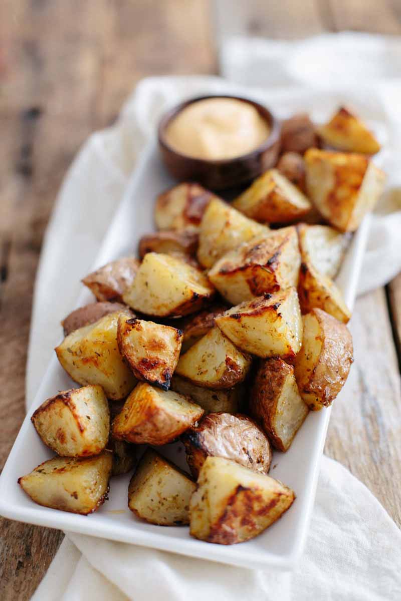 Vertical image of a platter of perfectly cooked potatoes with a bowl of sauce.