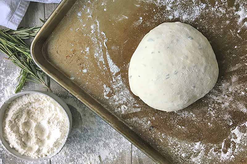 Horizontal image of a ball of dough on a floured baking sheet.