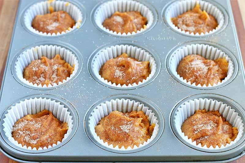 Orange muffin batter in a tin, topped with a sprinkling of cinnamon sugar.