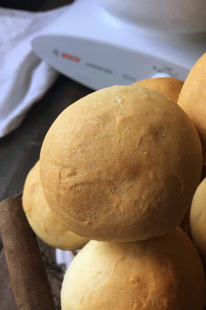 Vertical image of bread rolls with a kitchen machine in the background.