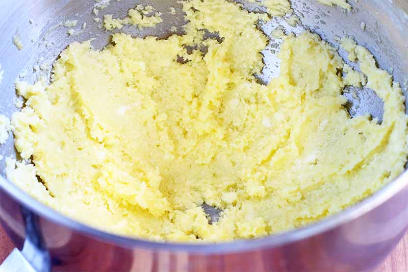 A thick yellow mixture that has just been beaten with an electric mixer is in the bottom of a stainless steel bowl.