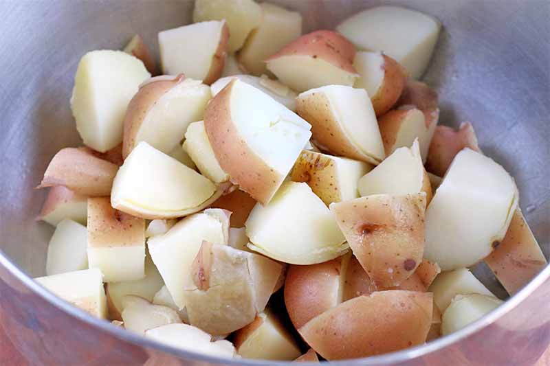 Boiled red-skinned potatoes cut into chunks in a stainless steel bowl.