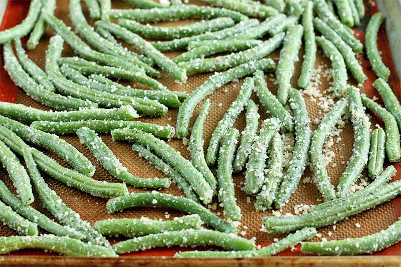 Green beans coated with grated parmesan cheese, spread in a single layer on a Silpat silicone pan liner.