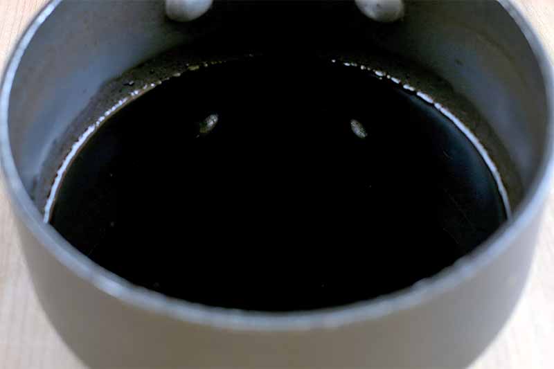 Closeup of a saucepan of balsamic vinegar reduction, on a beige surface.
