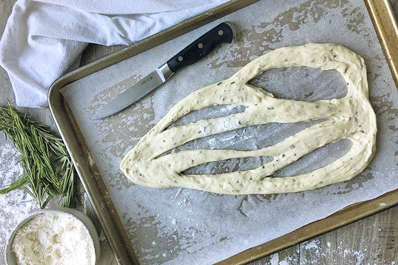 Horizontal image of sliced dough on a baking sheet with a knife and a bowl of flour.