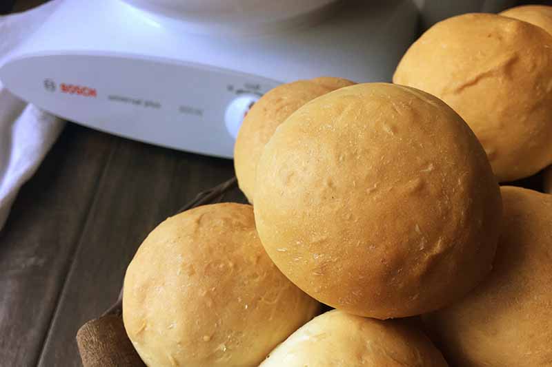 Horizontal image of a pile of bread rolls in front of kitchen equipment.