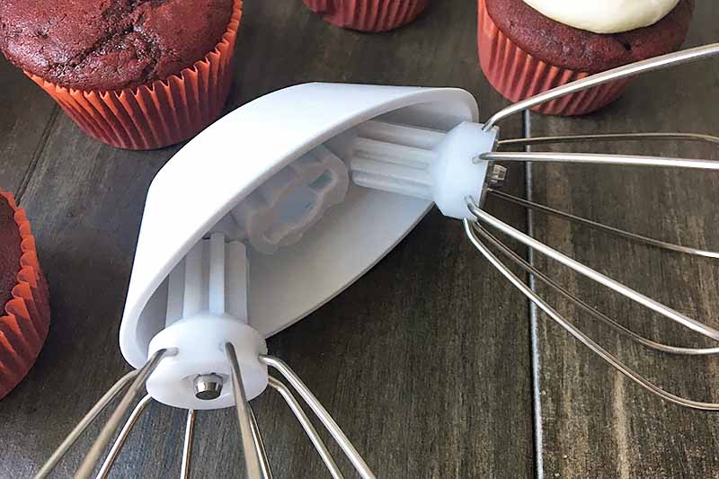 Horizontal image of wire whips attached to a plastic drive, with red cupcakes.