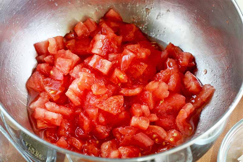 Chopped tomatoes in the bottom of a stainless steel mixer bowl.