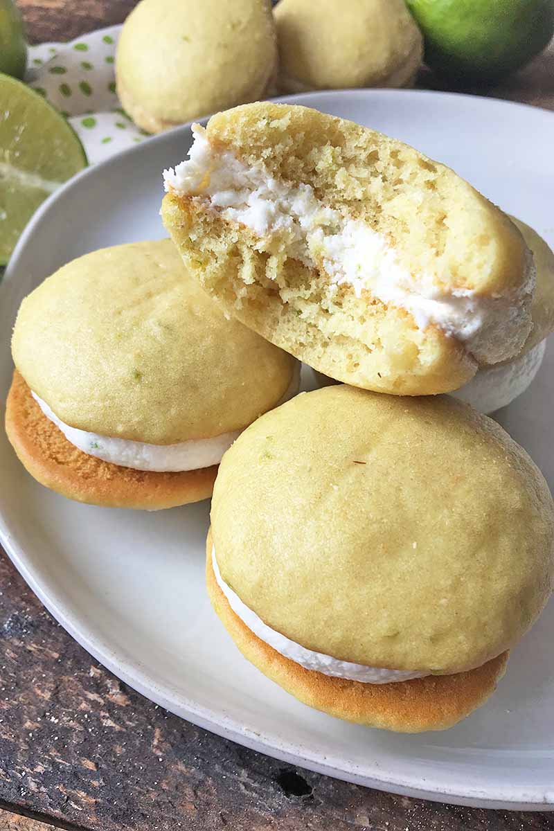 Vertical image of yellow whoopie pies on a white plate, one with a huge bite.