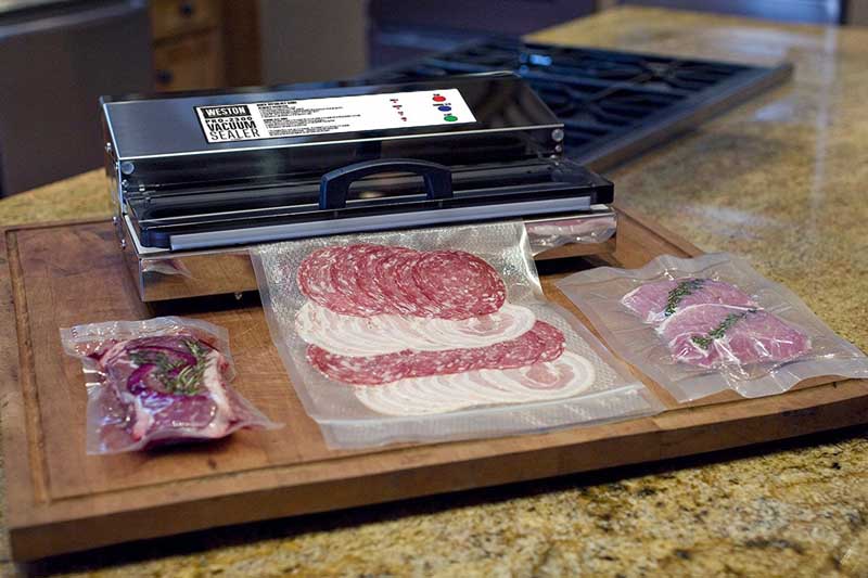 A photo of the Weston Pro 2300 vacuum sealer bagging cold cuts and other lunch meat on a large wooden cutting board.