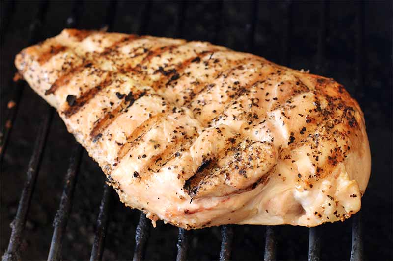 A piece of chicken breast coated with spices is grilling on metal grates.