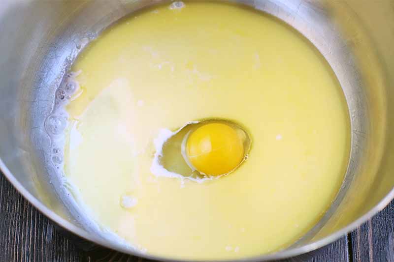 Overhead shot of an egg cracked into the middle of a yellow liquid mixture in a large stainless steel bowl.