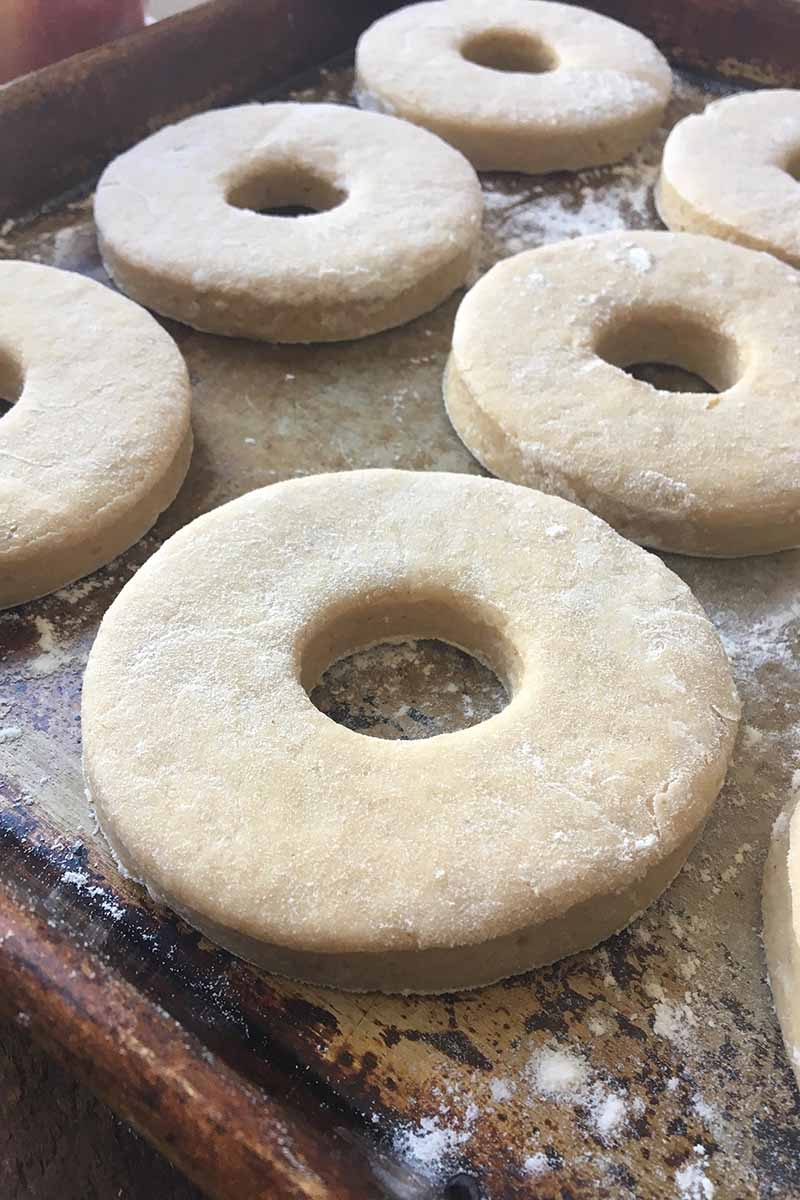 Vertical image of uncooked doughnuts on a baking sheet.